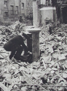 Postman collecting letters from a postbox surrounded by debris from world war 2
